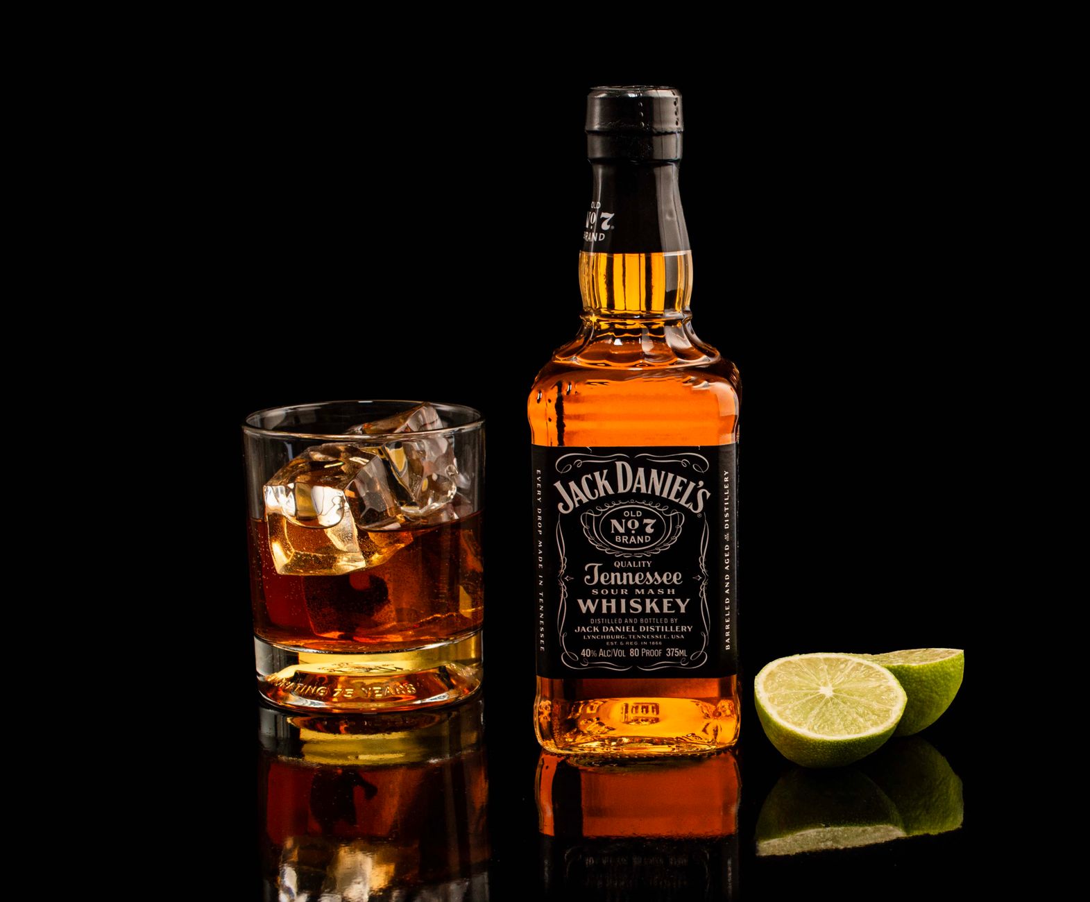 Butelka Jack Daniel’s i szklanka z limonką na czarnym, lśniącym blacie
