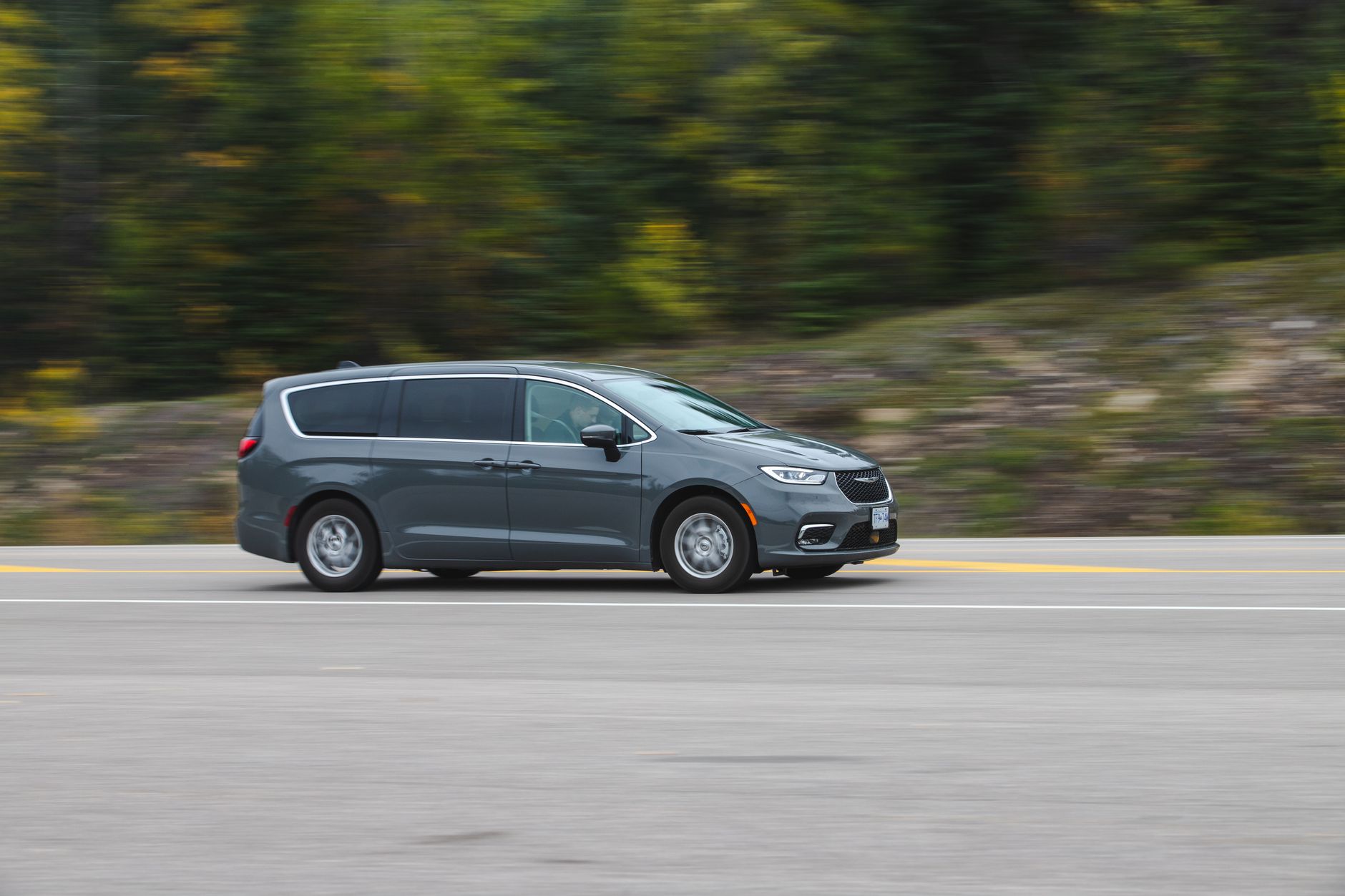 Volvo XC70 jako auto do firmy: koszty serwisu, spalanie i praktyczność w trasie Srebrne kombi jedzie po malowniczej trasie wśród zieleni