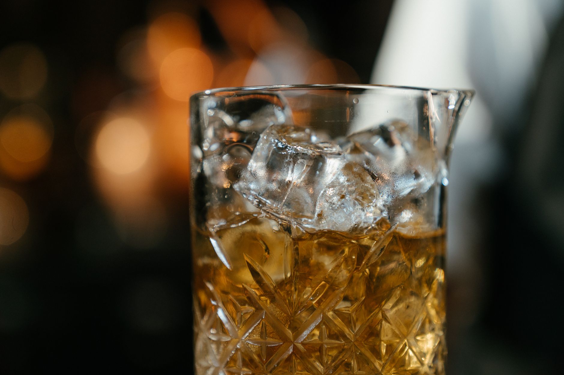 Szklane naczynie mikserskie z lodem i whisky na rozmytym tle